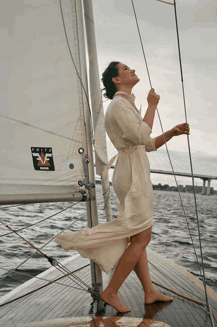 a woman in a white dress stands on a sailboat with a fritz vf sticker on the sail