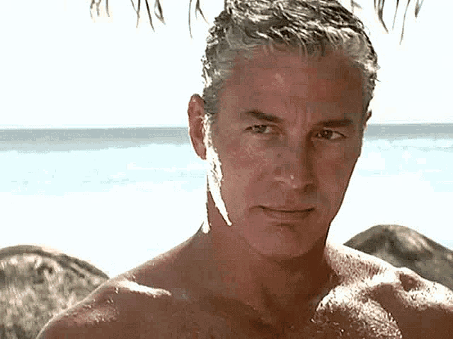 a man without a shirt is standing on the beach looking at the camera