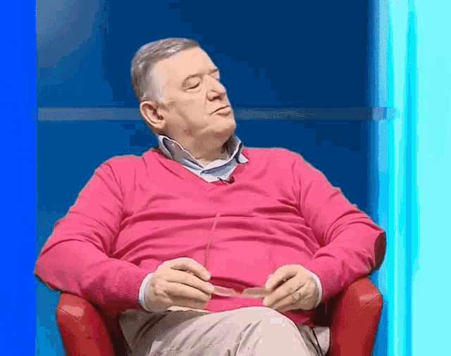 a man wearing a pink sweater is sitting in a red chair