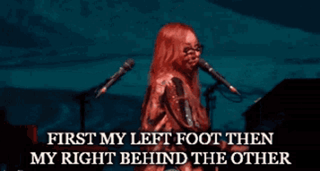 a red haired woman singing into a microphone with the words first my left foot then my right behind the other