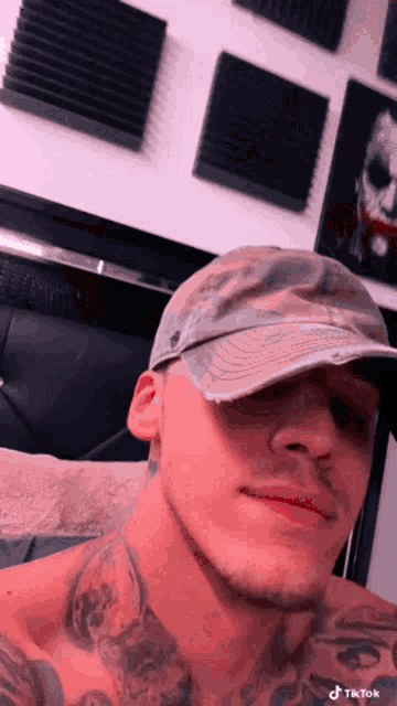 a shirtless man wearing a hat and a tattoo on his chest is taking a selfie .