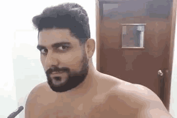 a shirtless man with a beard is taking a selfie in a bathroom .