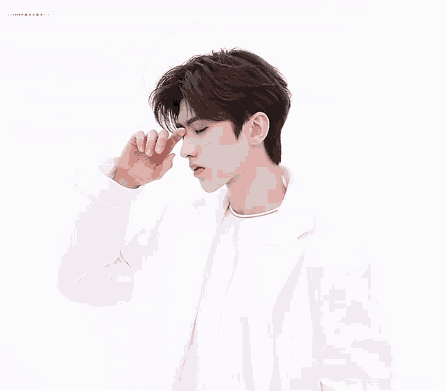 a young man in a white jacket is touching his face with his hand