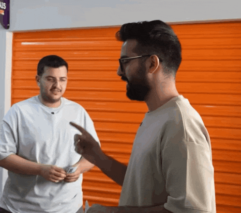 two men standing in front of an orange garage door with a sign that says ' us ' on it