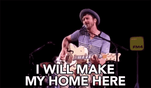 a man playing a guitar and singing into a microphone with the words " i will make my home here " above him