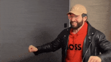 a man with a beard wearing a hat and a leather jacket .