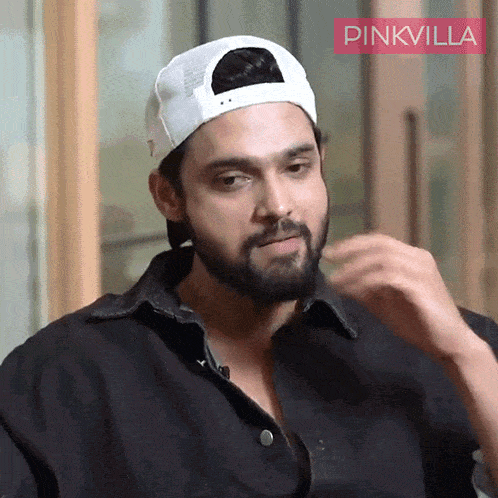 a man with a beard wearing a white baseball cap with pinkvilla written on the bottom