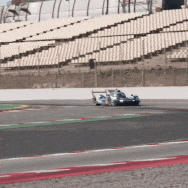 a race car is driving on a race track with empty bleachers in the background