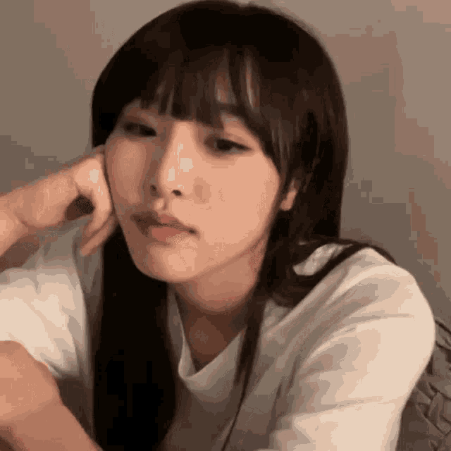 a woman with long hair and bangs is sitting down with her hand on her face .