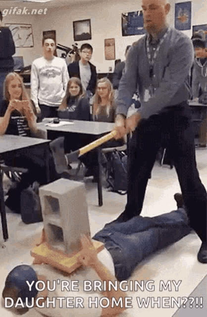 a man is hitting a man with a bat in a classroom while laying on the floor .