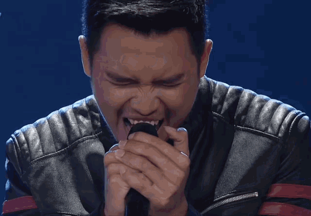 a man in a leather jacket is singing into a black microphone