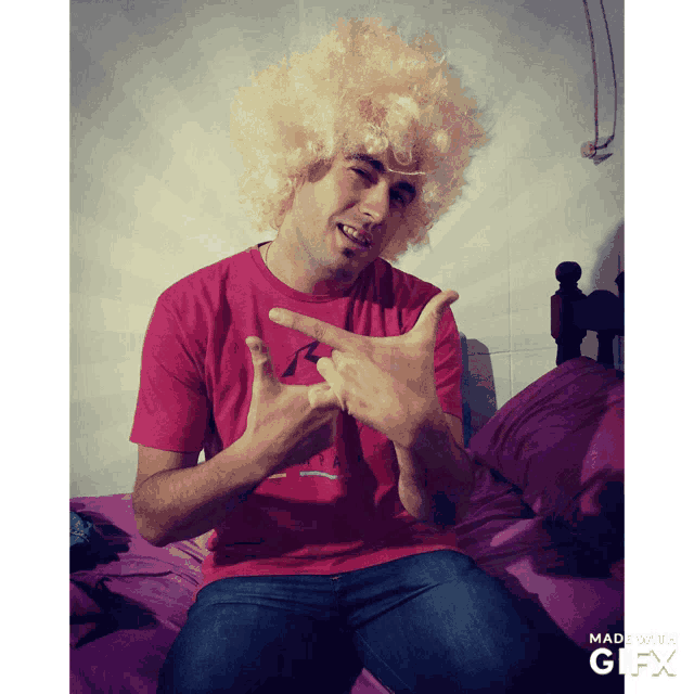 a man wearing a wig and a red shirt is sitting on a bed with a gifx watermark