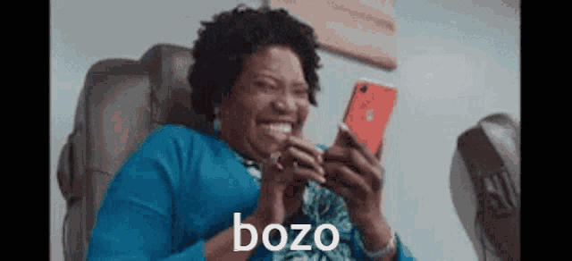 a woman is sitting in a chair looking at her phone and the word bozo is on the screen behind her