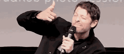 a man in a suit is holding a microphone and giving a thumbs up .