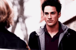 a man wearing a hoodie and a burgundy shirt looks at the camera