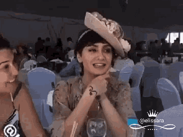 two women are sitting at a table with one wearing a hat