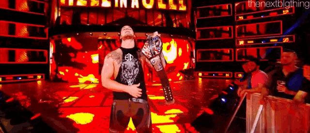 a wrestler is holding a wrestling championship belt in front of a crowd .