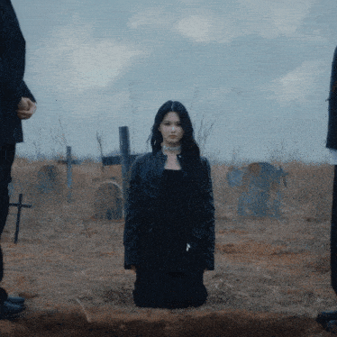 a woman in a black jacket is kneeling in a field of graves