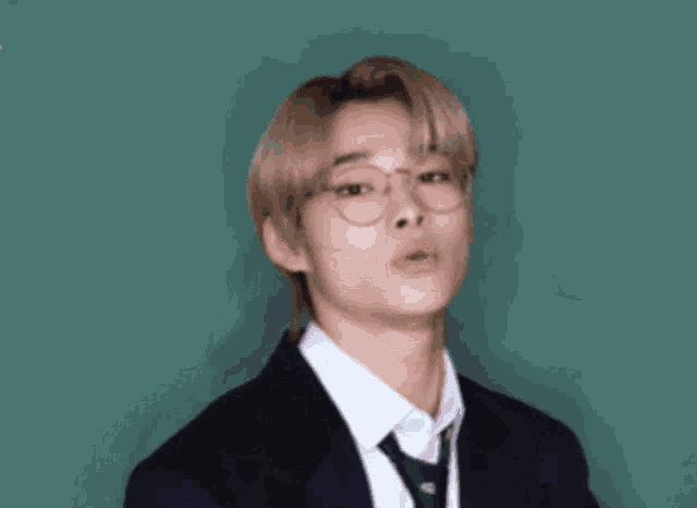 a young man wearing glasses and a suit is making an ok sign .