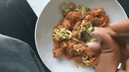 a person is eating a plate of food with noodles and meat on a table .