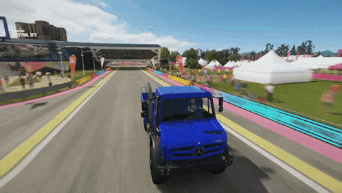 a blue mercedes truck is driving down a road in front of a festival site