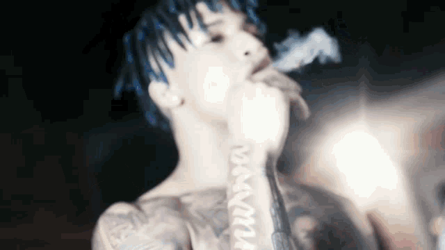 a man with blue hair is smoking a cigarette and has a tattoo on his arm