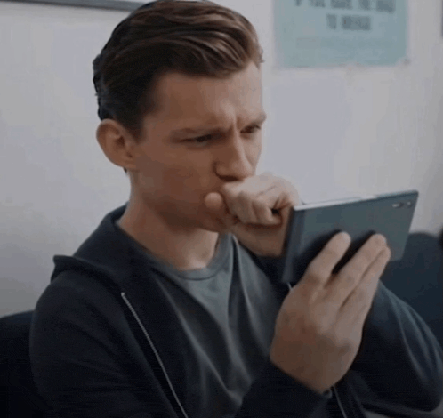 a man looking at a cell phone with a sign on the wall behind him