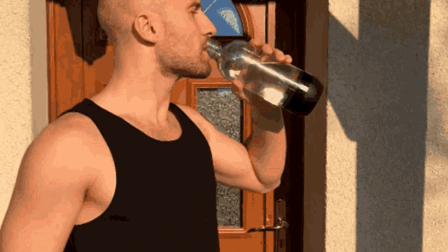 a man in a black tank top is drinking from a bottle