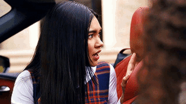 a woman in a plaid dress is sitting in the back seat of a car talking to a man .