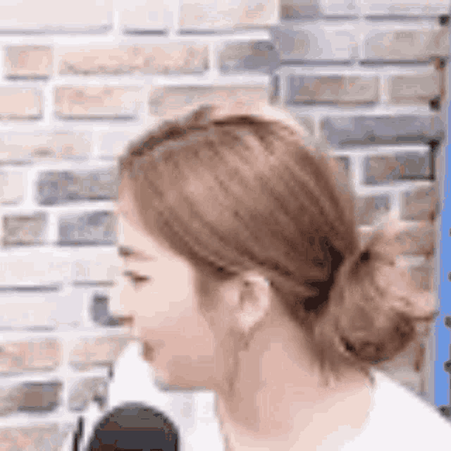 a woman with her hair in a bun is standing in front of a microphone .