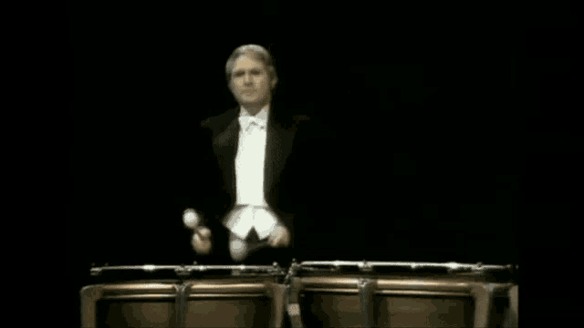 a man in a tuxedo is playing drums in front of a crowd while the drums are exploding .