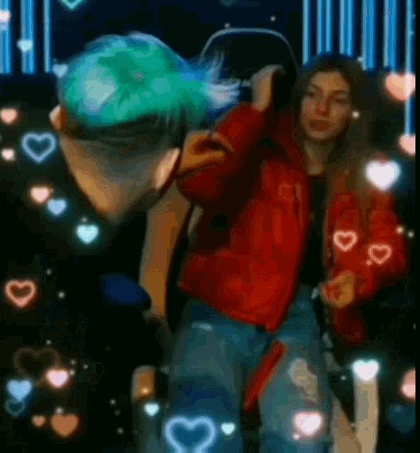a man with green hair and a woman in a red jacket are standing next to each other on a stage .