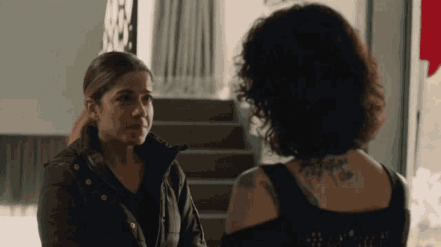 a woman with a tattoo on her back looks at another woman