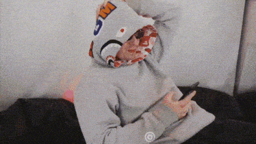 a person wearing a shark hoodie is sitting on a couch and looking at their phone .