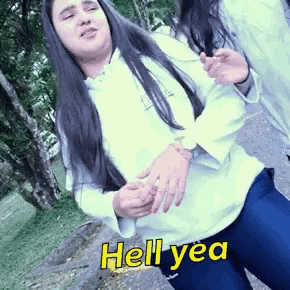 a girl with long hair is wearing a white shirt and blue jeans and says hell yea in yellow letters .