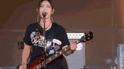 a woman is singing into a microphone while playing a guitar and wearing a shirt that says over