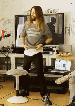 a man with long hair is dancing in a living room
