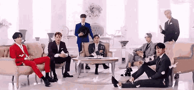 a group of men in suits are sitting on couch and chairs in a living room .