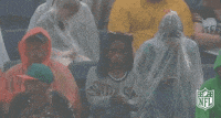 a group of people are sitting in a stadium wearing plastic raincoats and covering their faces .