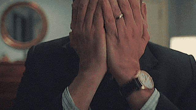 a man in a suit is covering his face with his hands while wearing a watch .