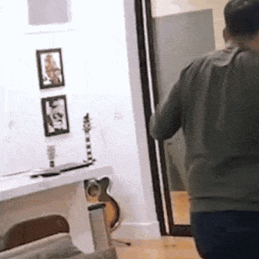 a man is standing in a living room with a guitar on the floor .