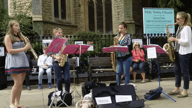 a group of women playing saxophones in front of a holy trinity church