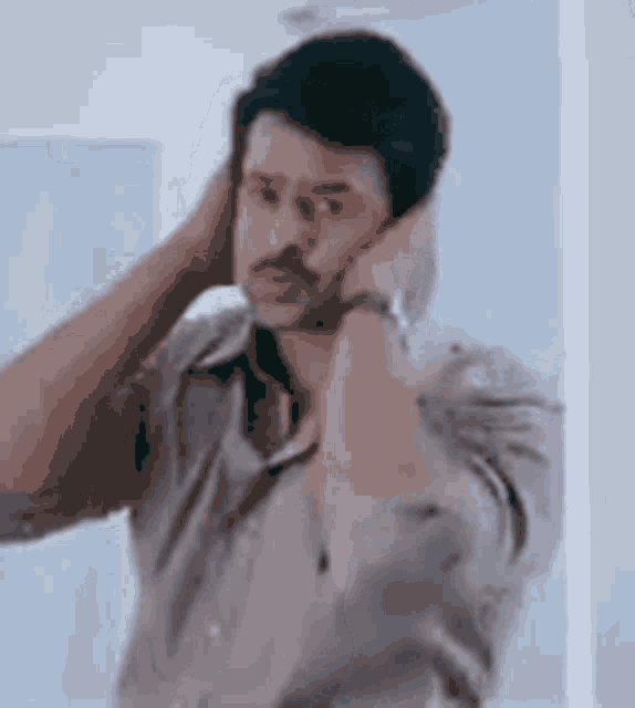 a man is covering his ears with his hands while looking at himself in a mirror .