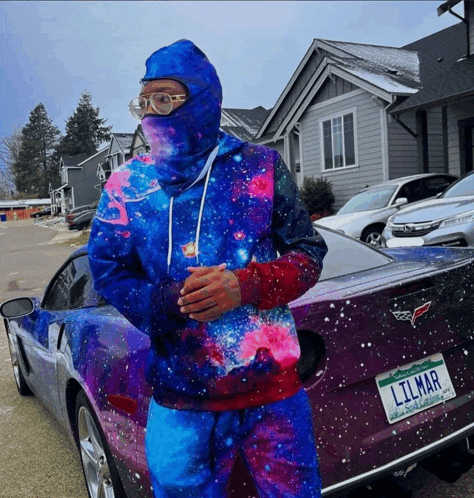 a man in a galaxy hoodie stands next to a purple car with a license plate that says lilmar