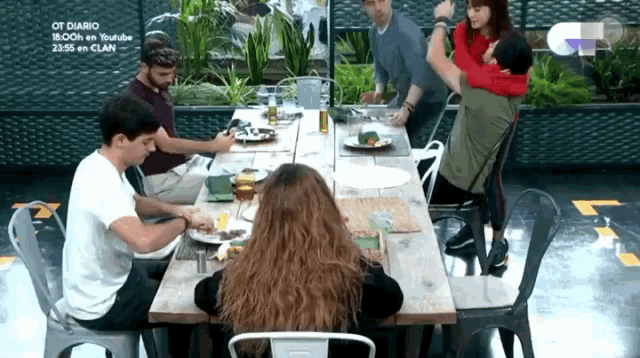 a group of people are sitting at a long table with plates of food on it .