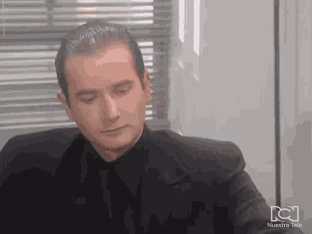 a man in a suit and tie is sitting in front of a window with nuestra tele written on the bottom right