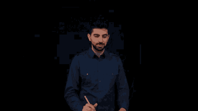 a man in a blue shirt is smiling while holding a pen in his hand