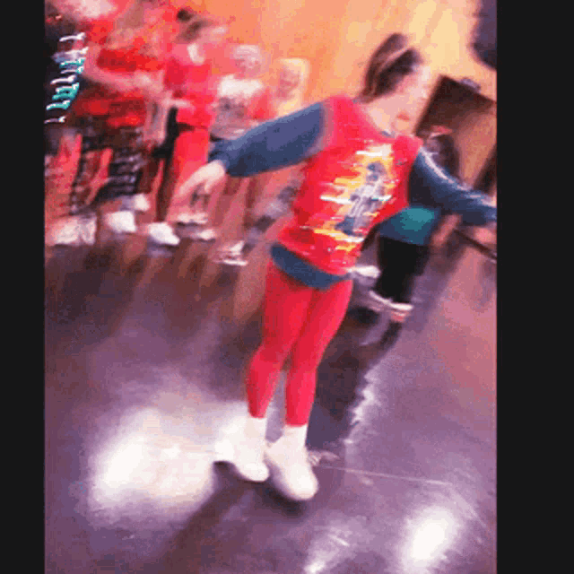 a girl in a red shirt and red leggings is dancing in a room