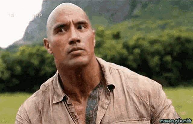 a bald man with a tattoo on his chest is standing in a field looking up .