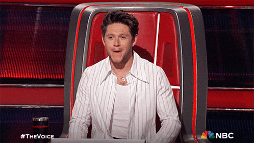 a man in a striped shirt is sitting in a chair with a nbc logo behind him